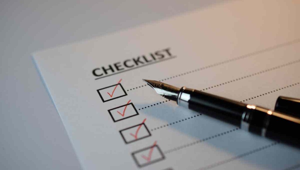 monthly bookkeeping checklist with red checkmarks and a pen on top of the paper.
