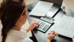 Woman using a calculator and reviewing financial documents at her desk, representing bookkeeping and accounting support services